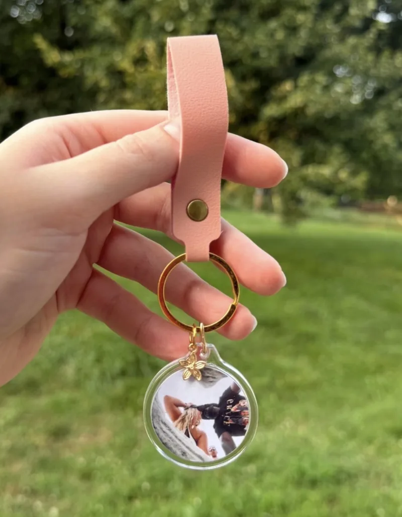 Hand holding a round custom photo keychain with a blush-pink strap