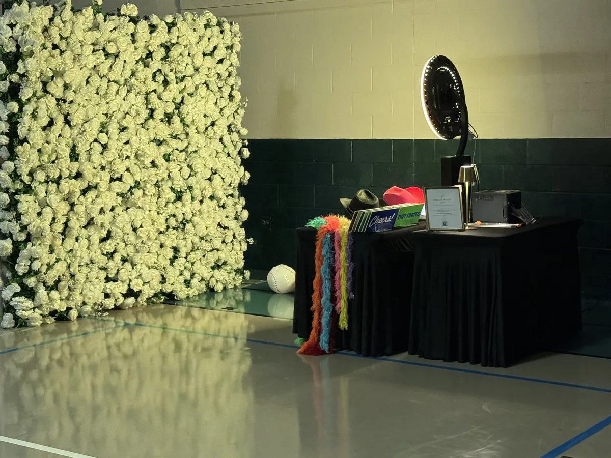 Photo booth ring light and prop table arranged beside a white floral wall